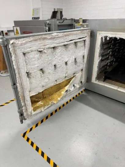 Heat treatment oven door with worn, damaged insulation lining before repair
